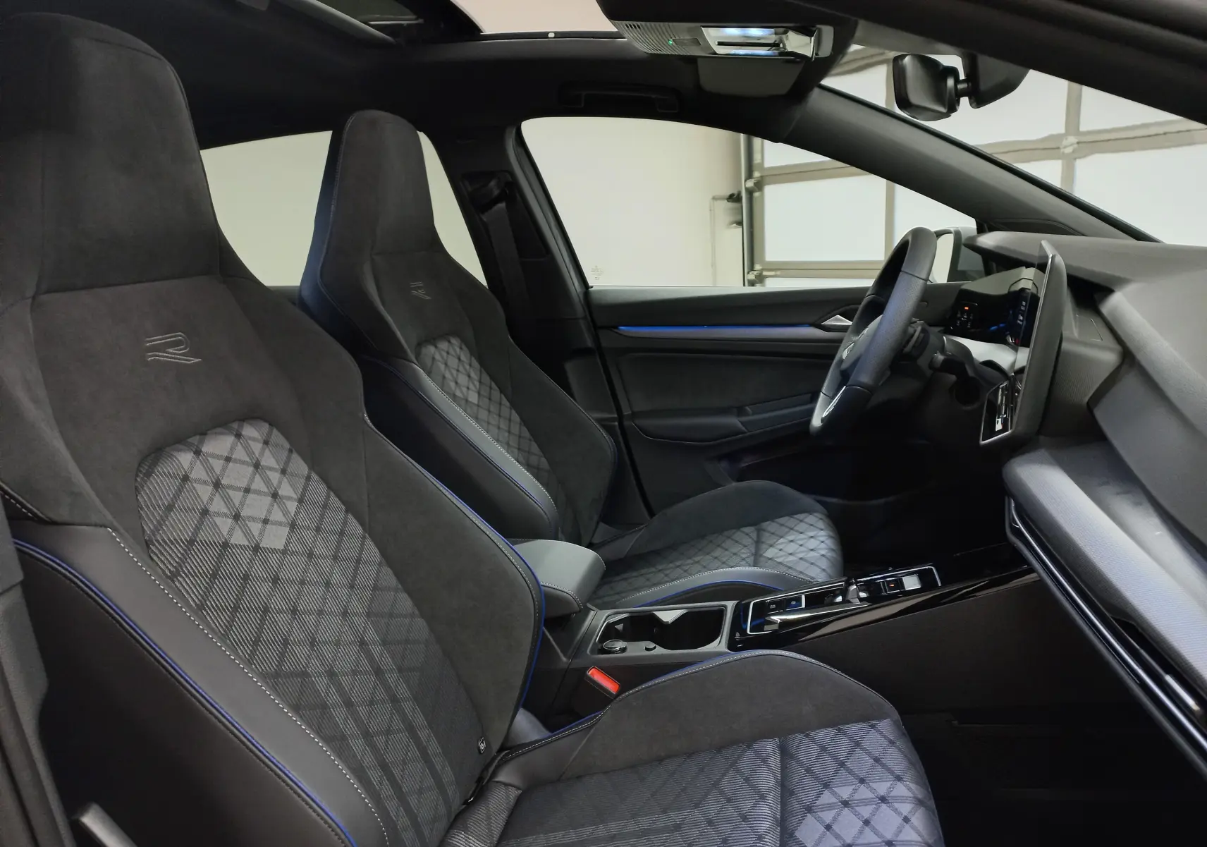 Vue intérieure côté conducteur de la Volkswagen Golf 2.0 TDI R-Line 2026, sièges sport noirs avec surpiqûres bleues et toit ouvrant.