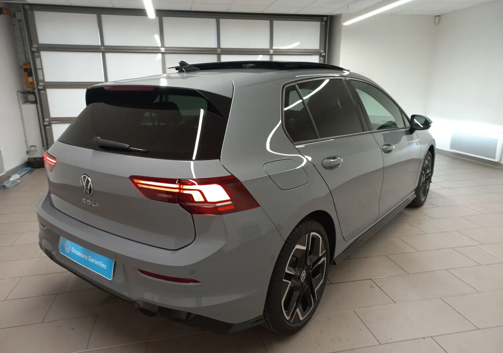 Vue 3/4 arrière droite d'une Volkswagen Golf 2.0 TDI gris lunaire avec toit ouvrant panoramique en intérieur.