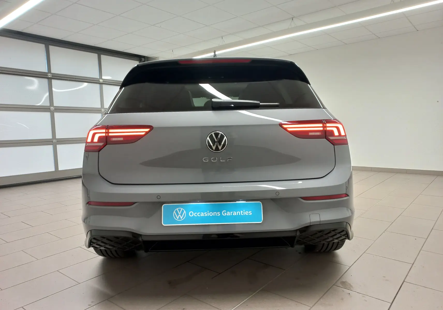 Vue arrière d'une Volkswagen Golf 2.0 TDI R-Line gris lunaire avec feux LED allumés dans un showroom.