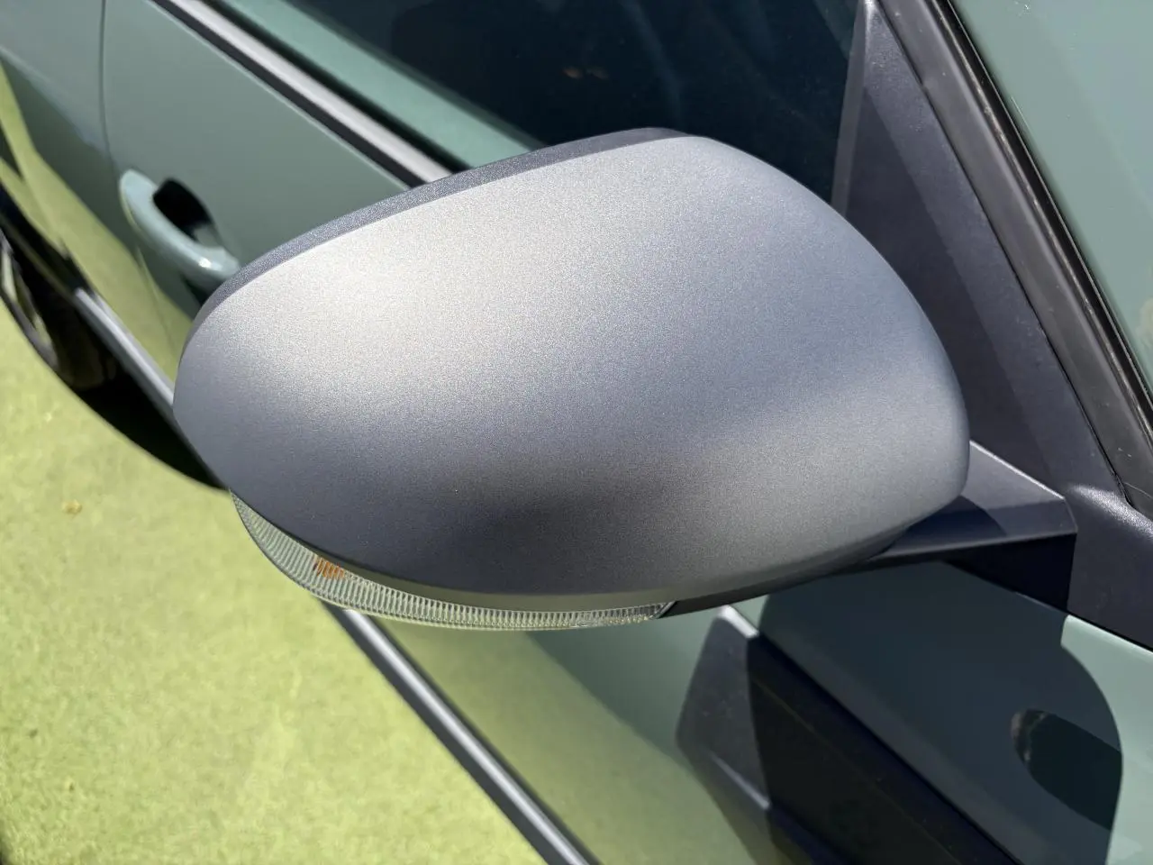 Gros plan sur le rétroviseur côté gauche gris mat du Dacia Duster III kaki lichen, avec clignotant intégré.