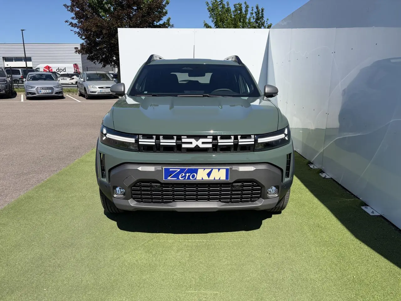 Vue de face du Dacia Duster III hybride en kaki lichen avec calandre noire et signature lumineuse LED fine.
