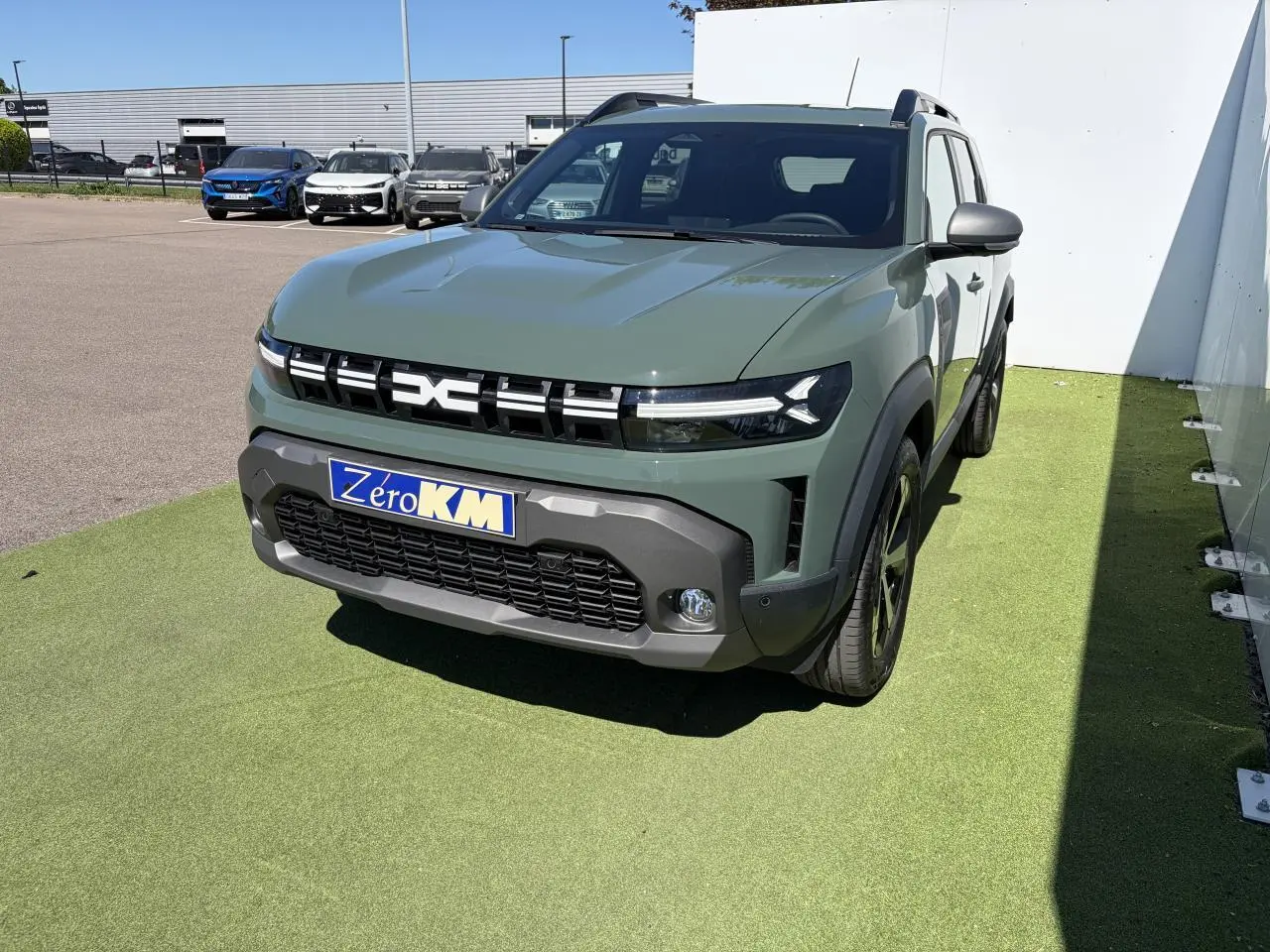 Vue 3/4 avant droit d'un Dacia Duster III hybride 2026 en kaki lichen avec calandre noire et jantes alliage 18 pouces.