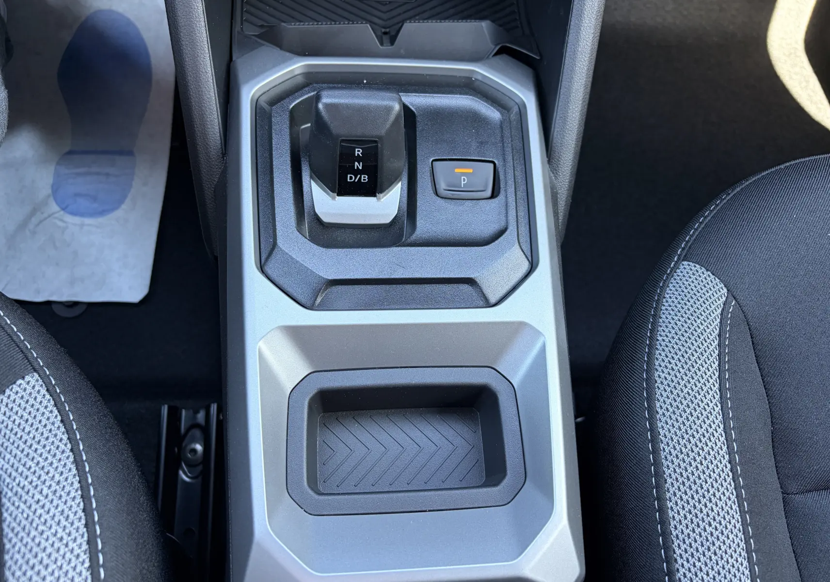 Vue plongeante sur la console centrale du Dacia Duster III hybride, avec levier de boîte auto et bouton de frein à main électrique.