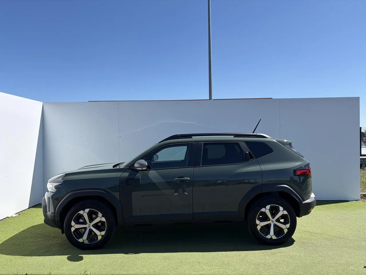 Vue de profil côté gauche du Dacia Duster III hybride 2026 en kaki lichen avec jantes alliage 18 pouces diamantées.