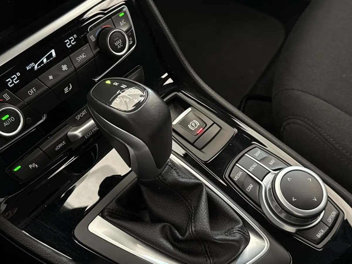 Gros plan sur la console centrale noire avec levier de vitesses et commandes multimédia d'une BMW Série 2 Active Tourer gris foncé.