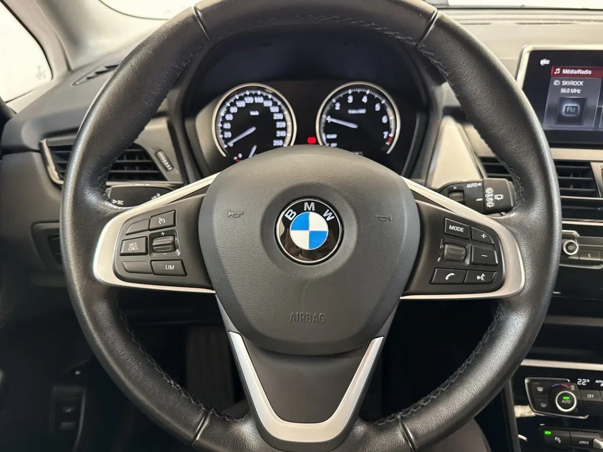 Vue rapprochée du volant cuir noir de la BMW Série 2 Active Tourer 225xe avec tableau de bord et écran tactile visibles.