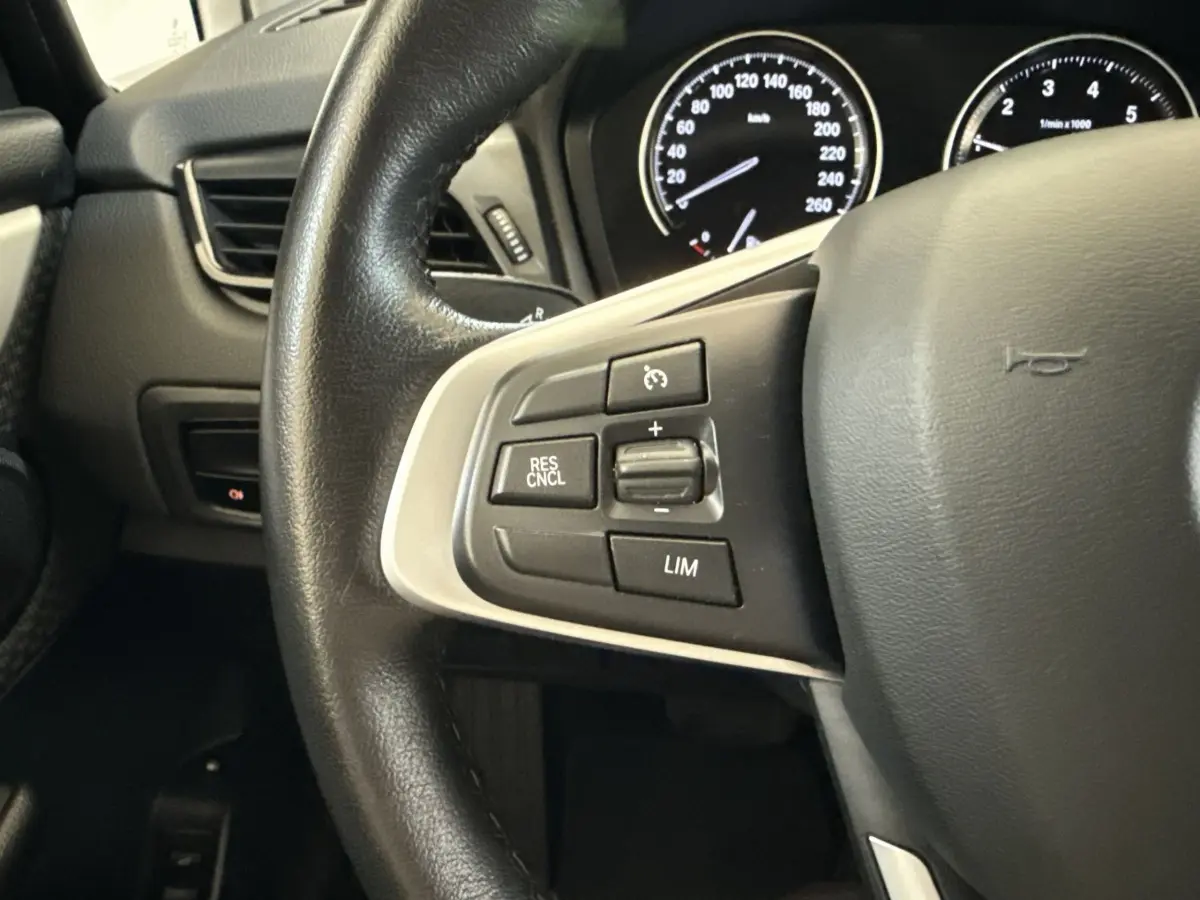 Gros plan sur le volant cuir noir de la BMW Série 2 Active Tourer 225xe avec commandes de régulateur de vitesse.