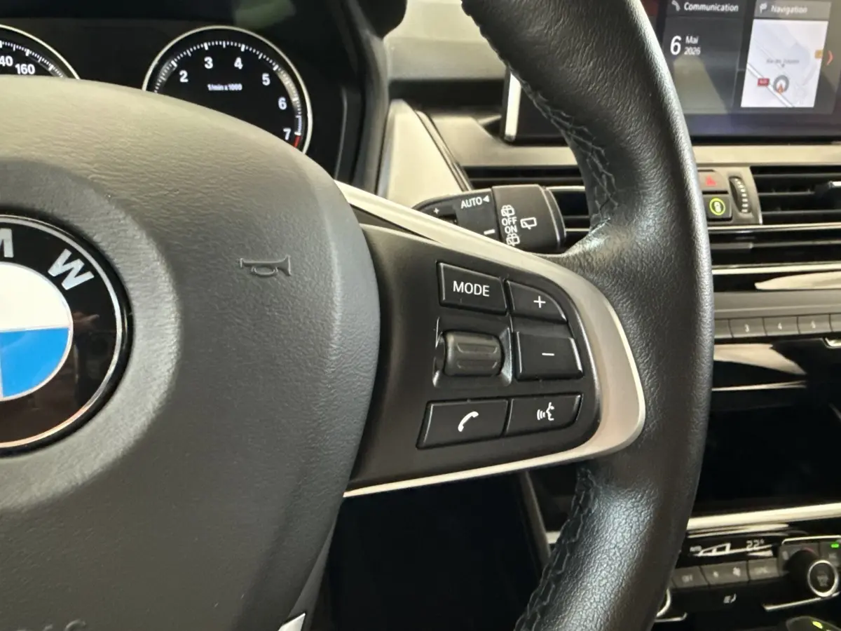Gros plan sur le volant cuir noir de la BMW Série 2 Active Tourer 225xe, avec commandes multifonctions visibles et tableau de bord en arrière-plan.