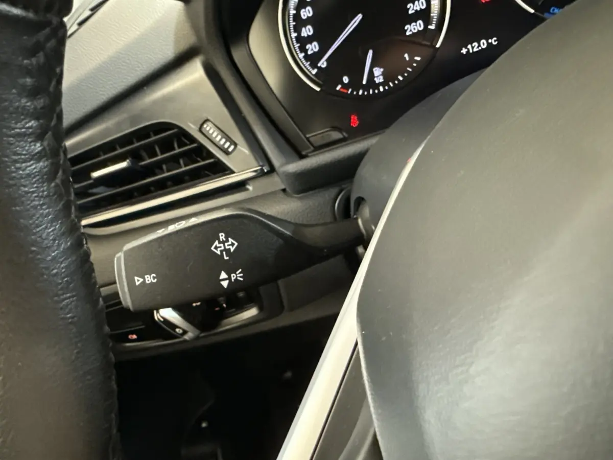 Gros plan sur le commodo de clignotant noir à gauche du volant dans l’habitacle d’une BMW Série 2 Active Tourer gris foncé.