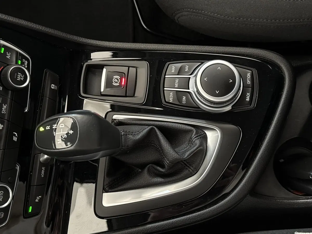 Gros plan sur la console centrale noire brillante de la BMW Série 2 Active Tourer 225xe avec levier de vitesse automatique et molette de contrôle.