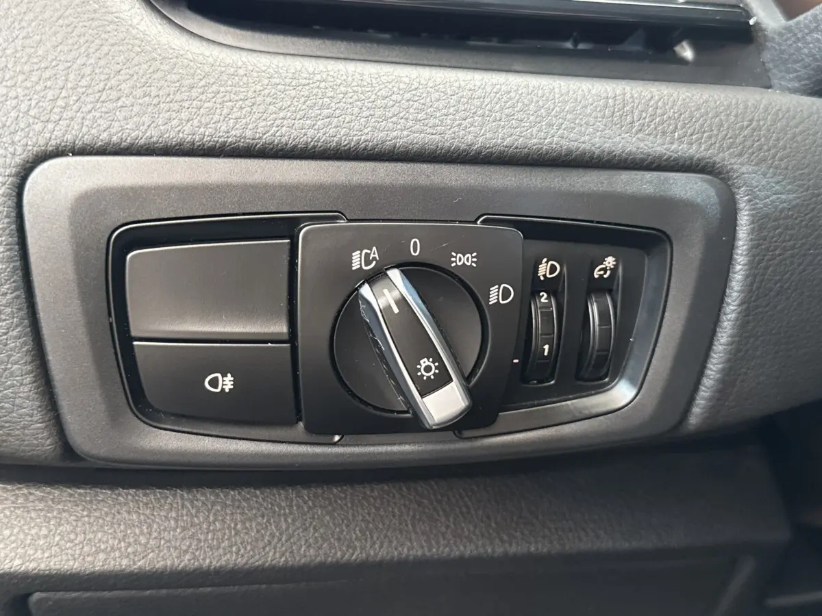 Gros plan sur le bouton de commande des phares et réglages lumineux dans l’habitacle d’une BMW Série 2 Active Tourer gris foncé.