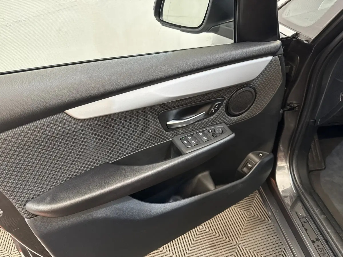 Vue intérieure côté gauche de la porte avant gris foncé d’une BMW Série 2 Active Tourer avec garniture carbone et commandes électriques.