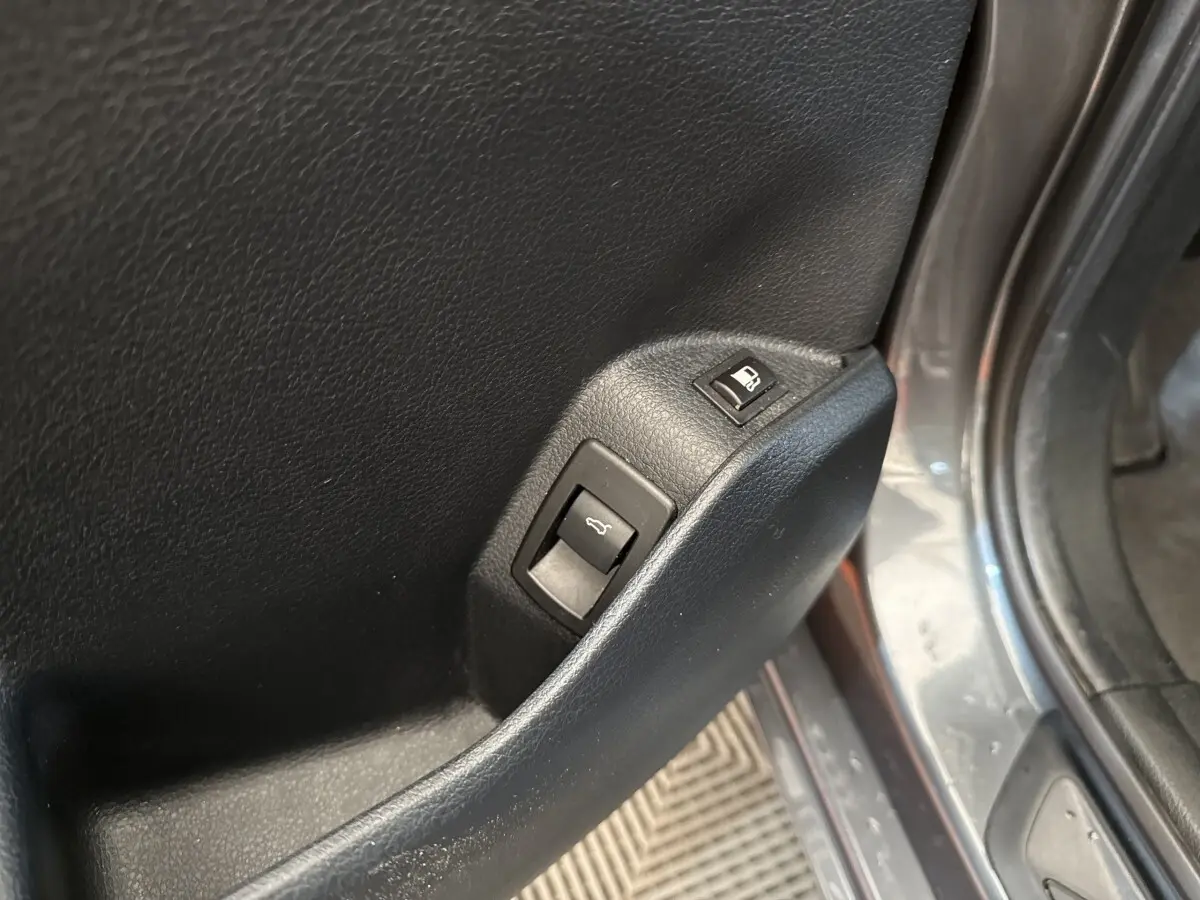 Gros plan sur les commandes d'ouverture du coffre et de la trappe à carburant sur la porte côté conducteur d'une BMW Série 2 Active Tourer gris foncé.