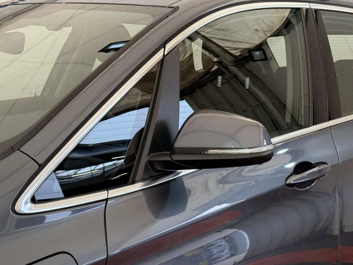 Gros plan sur le côté gauche gris foncé d'une BMW Série 2 Active Tourer avec rétroviseur et poignée de porte visibles.