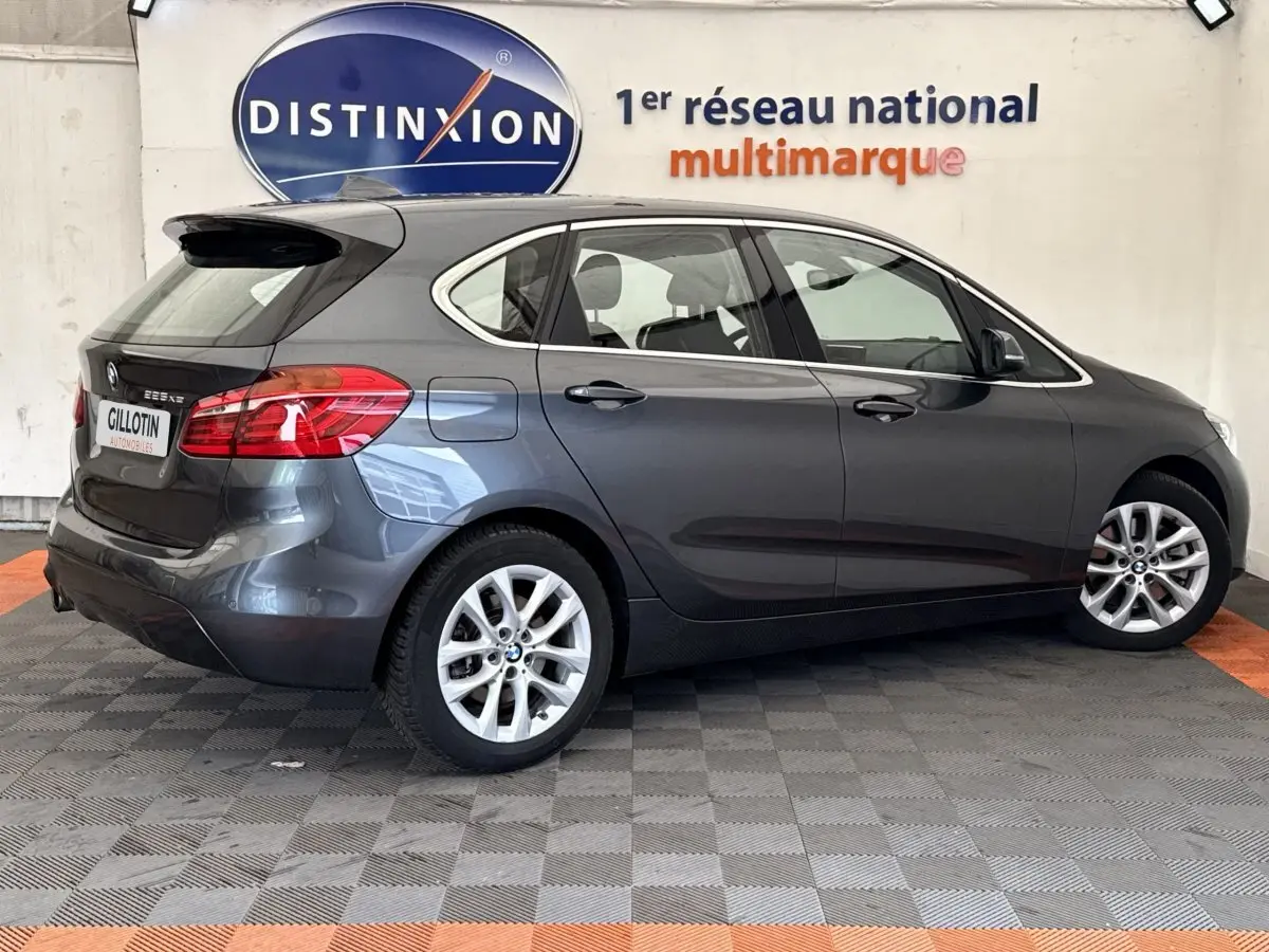BMW Série 2 Active Tourer 225xe gris foncé vue de profil droit en intérieur avec logo Distinxion en arrière-plan.