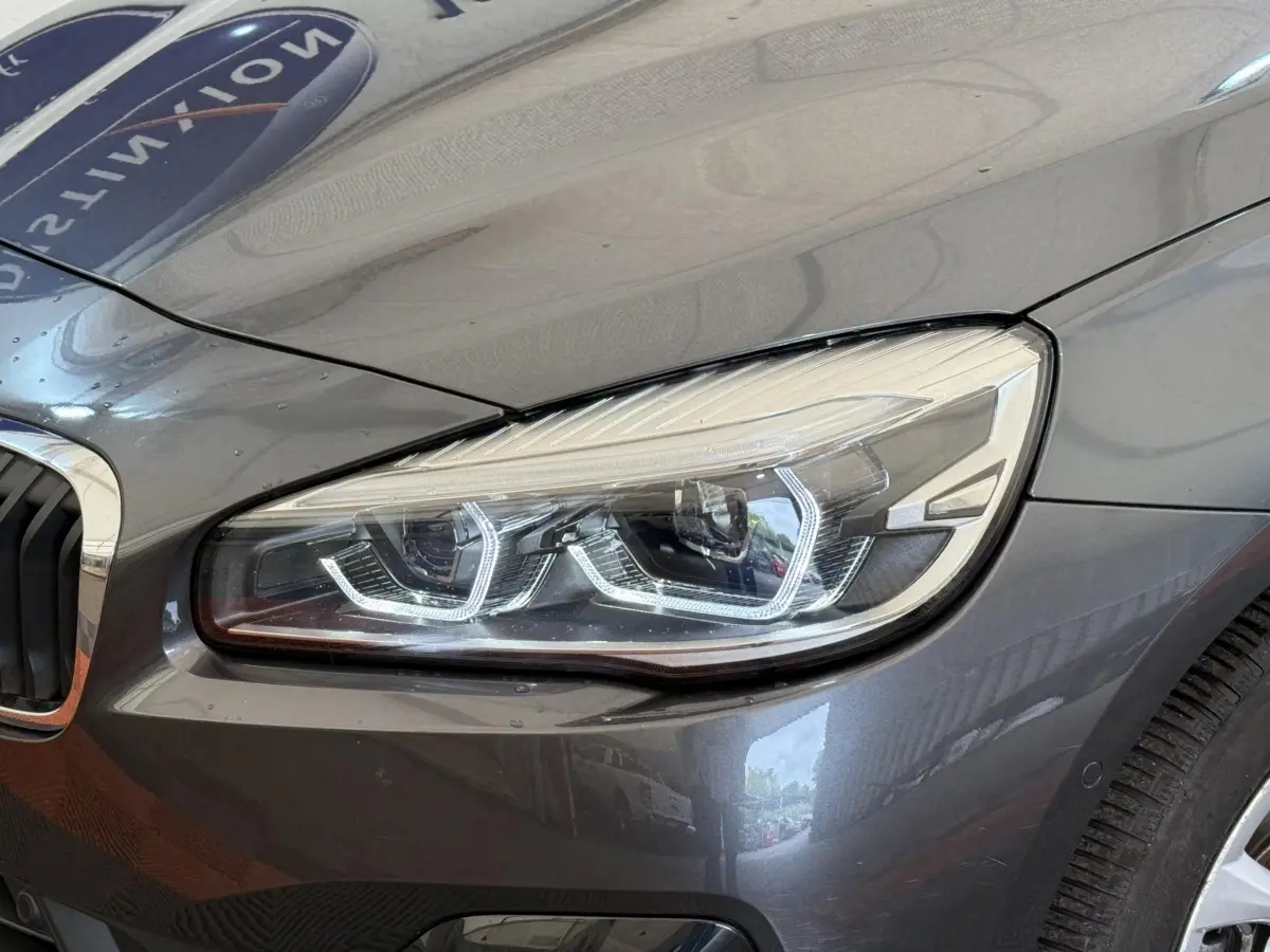 Gros plan sur le phare avant droit d'une BMW Série 2 Active Tourer gris foncé avec détails LED distinctifs.