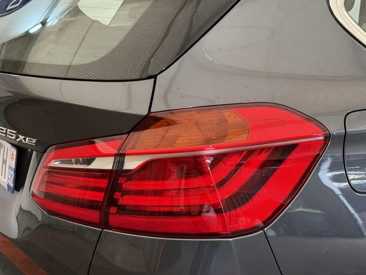 Gros plan sur le feu arrière droit rouge et orange d'une BMW Série 2 Active Tourer gris foncé, version 225xe.