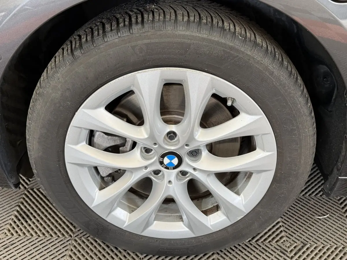 Gros plan sur la roue avant gauche avec jante argentée et logo BMW sur véhicule gris foncé.