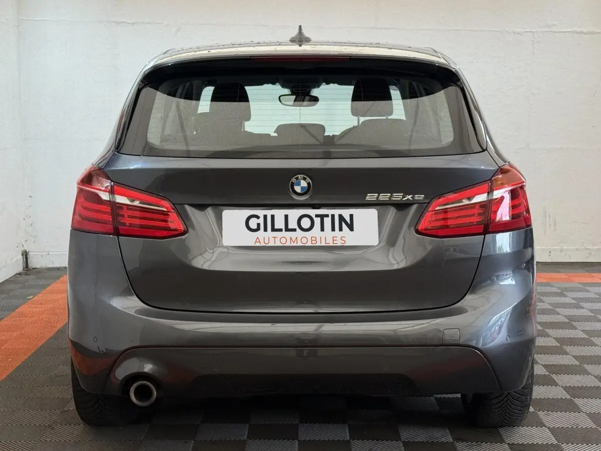 Vue arrière d'une BMW Série 2 Active Tourer 225xe gris foncé avec feux rouges et logo visible sur fond neutre.