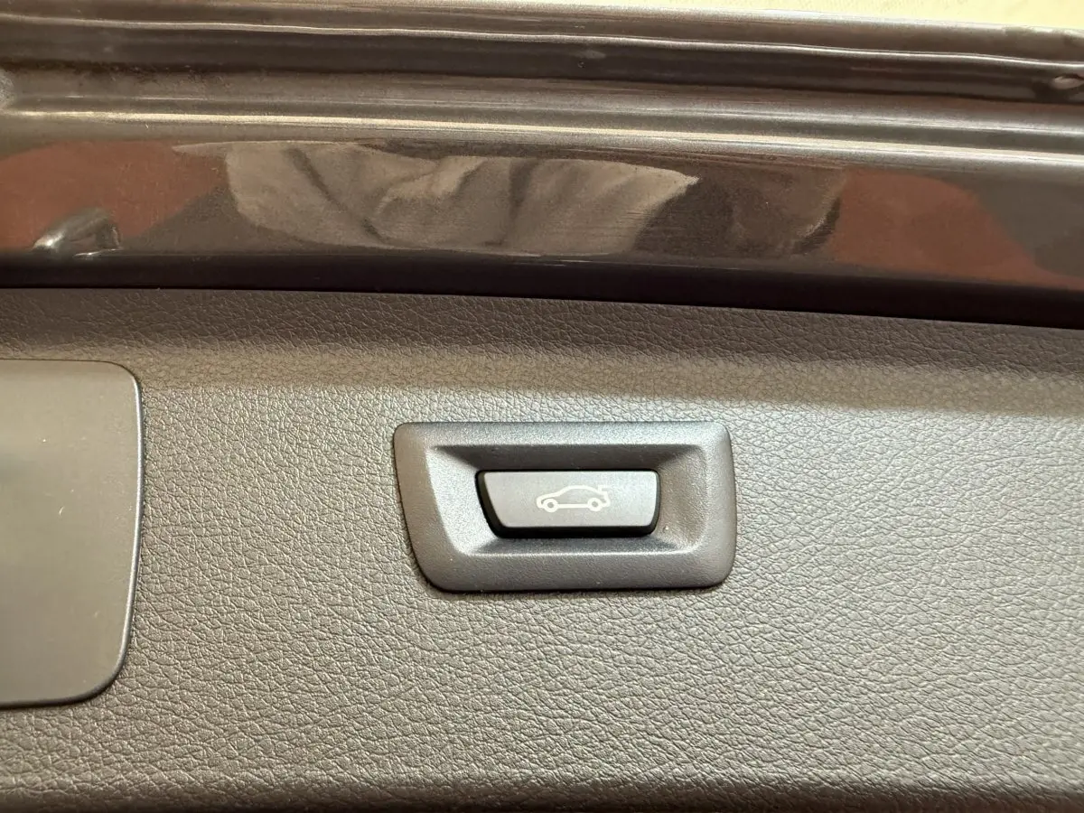 Gros plan sur le bouton d'ouverture électrique du coffre, intérieur noir texturé de la BMW Série 2 Active Tourer gris foncé.