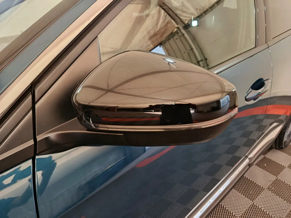 Gros plan sur le rétroviseur côté gauche noir brillant d'un Peugeot 3008 bleu, avec reflet de l'environnement intérieur.
