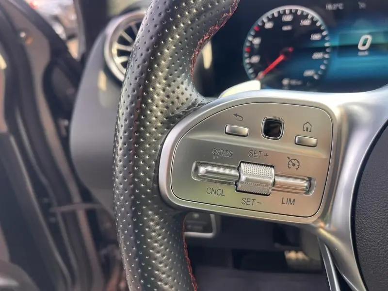 Gros plan sur le volant cuir perforé côté gauche du Mercedes GLA 200 d AMG Line gris montagne magno avec commandes intégrées.