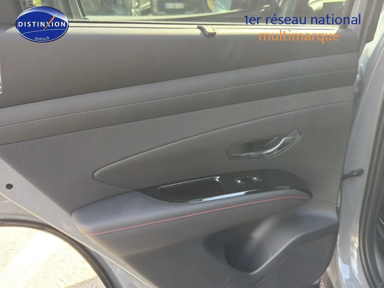 Vue intérieure de la porte arrière droite gris shadow du Hyundai Tucson 2026 avec surpiqûres rouges et commandes de vitres.
