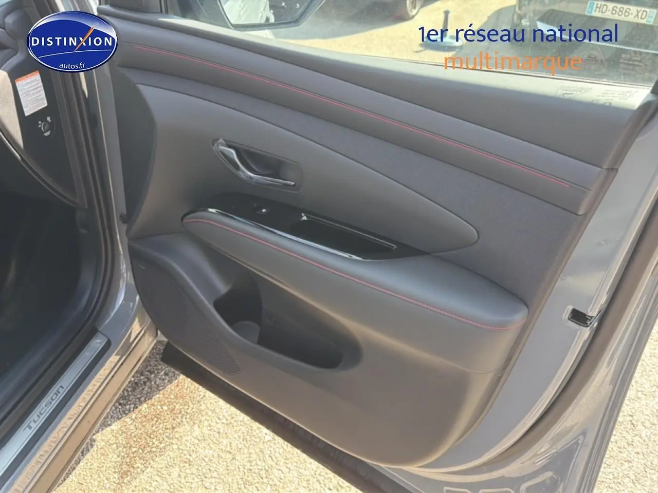 Vue intérieure de la porte avant gauche du Hyundai Tucson gris shadow avec surpiqûres rouges et poignée chromée.