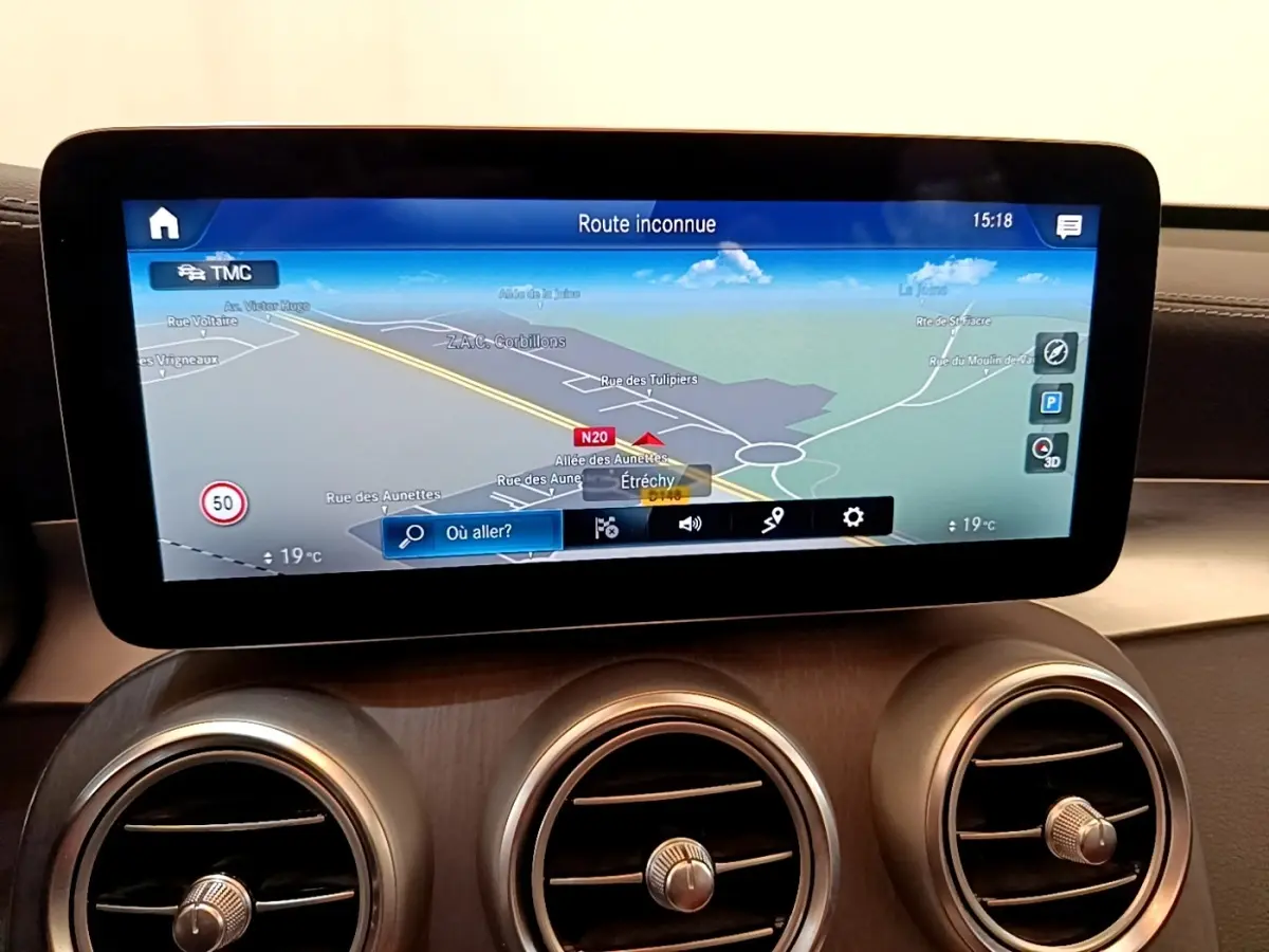 Écran tactile du système de navigation affichant une carte, avec trois aérateurs ronds en dessous, intérieur cuir marron.