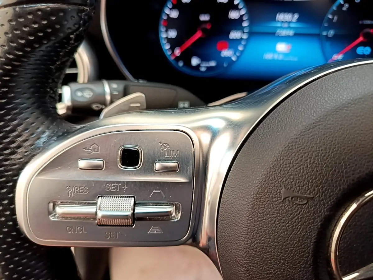 Gros plan sur les commandes du volant cuir et alu du Mercedes GLC 300 e AMG Line, affichage numérique en arrière-plan.