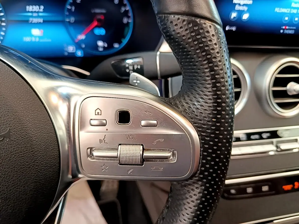 Gros plan sur le volant cuir perforé côté gauche du Mercedes GLC 300 e AMG Line, avec commandes intégrées et tableau de bord digital.