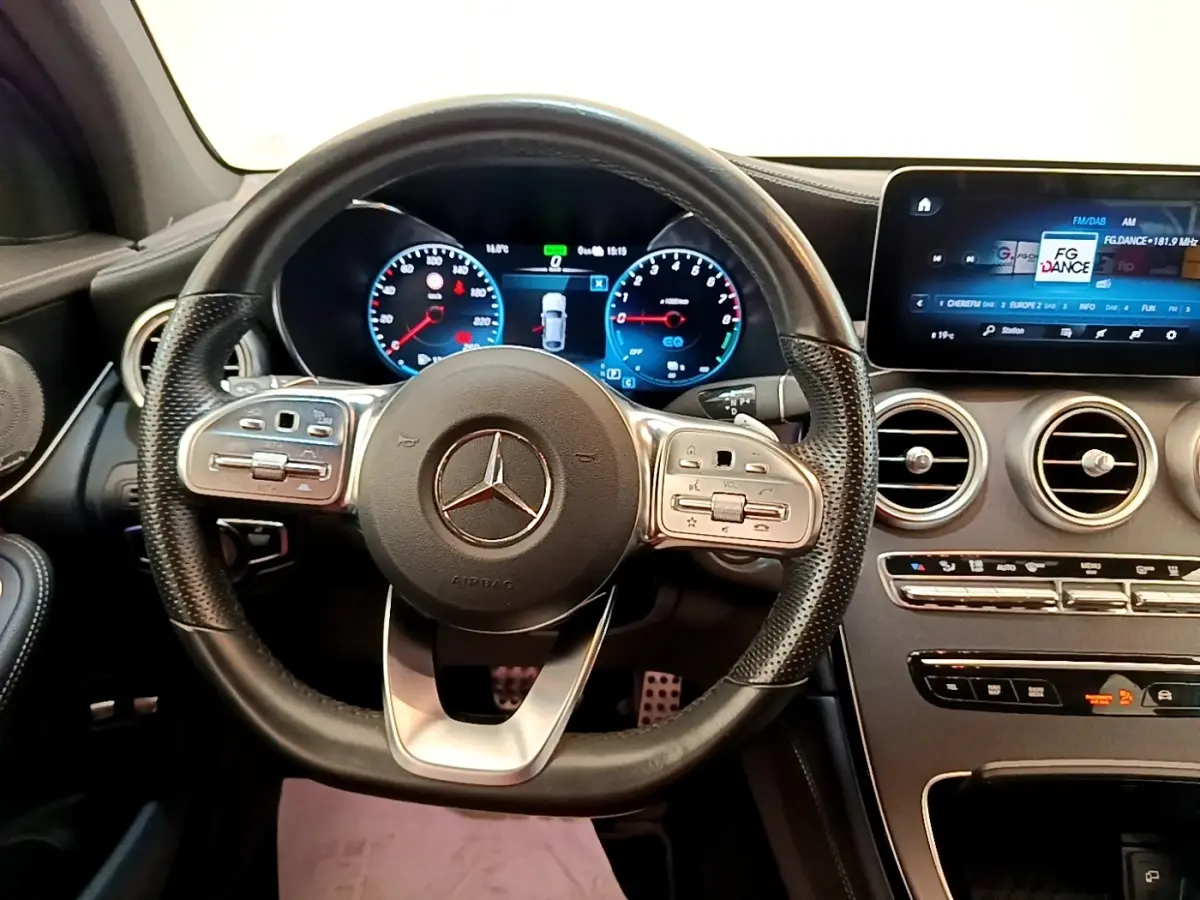 Vue intérieure centrée sur le volant cuir AMG et le tableau de bord numérique du Mercedes GLC 300 e blanc de 2020.