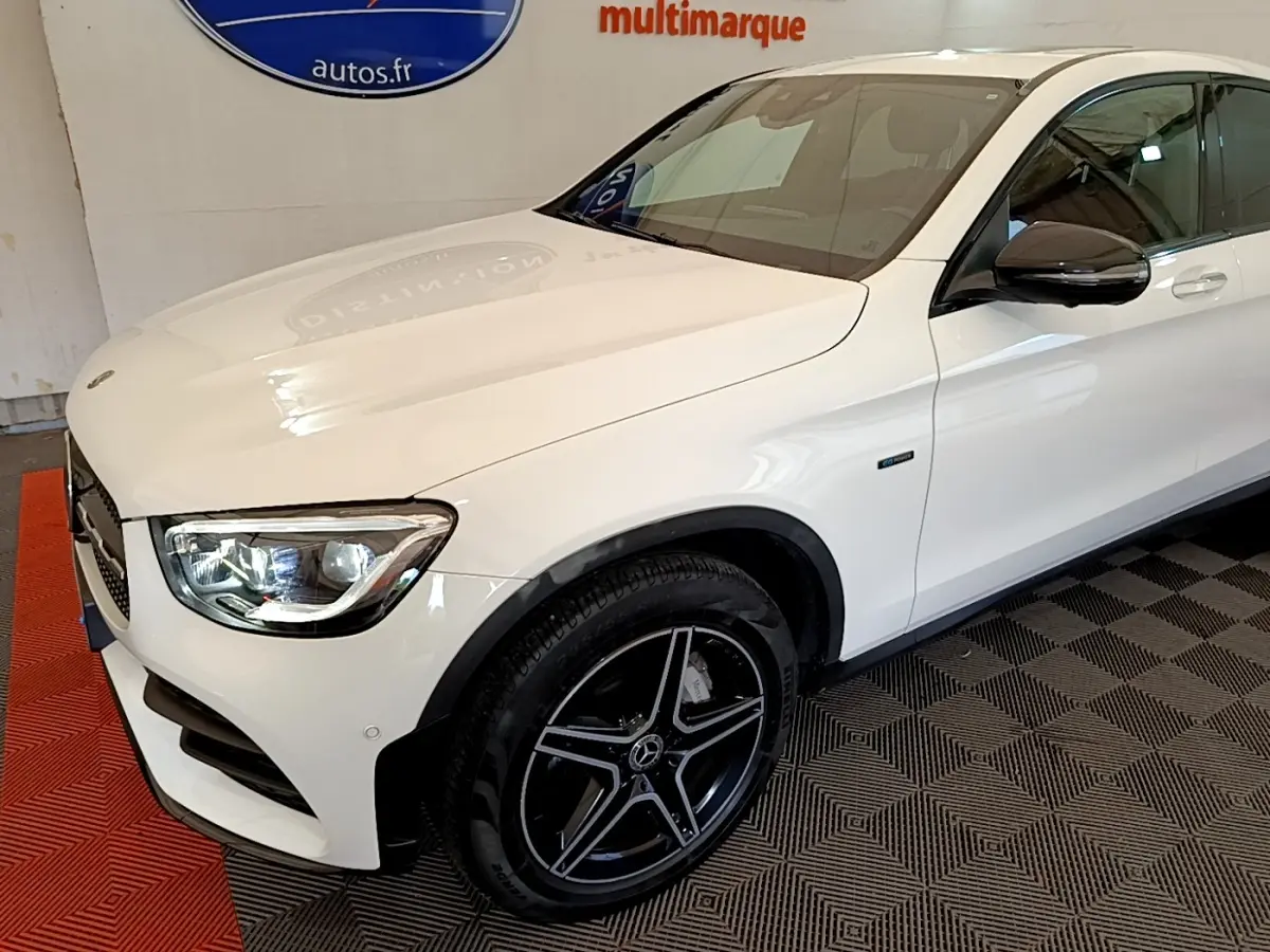 Mercedes GLC 300 e AMG Line blanc vu de 3/4 avant droit, avec jantes noires et phares LED allumés.