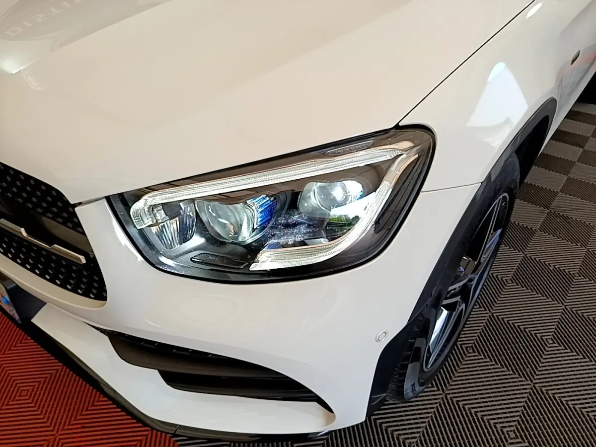 Gros plan sur l'avant droit blanc du Mercedes GLC Coupé 300 e AMG Line, mettant en valeur le phare LED et la jante noire.