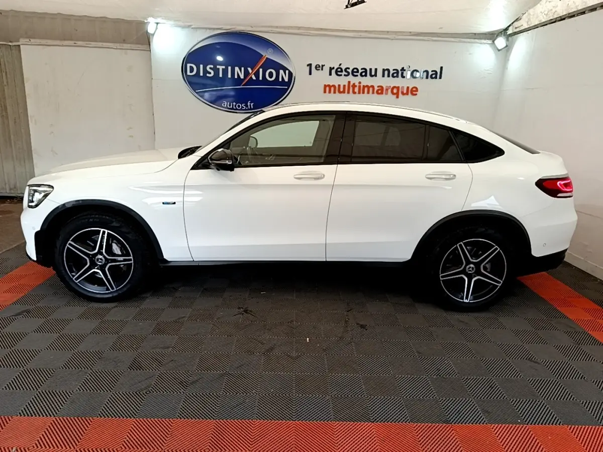 Profil droit d’un Mercedes GLC Coupé blanc hybride rechargeable avec jantes AMG et feux arrière LED allumés.