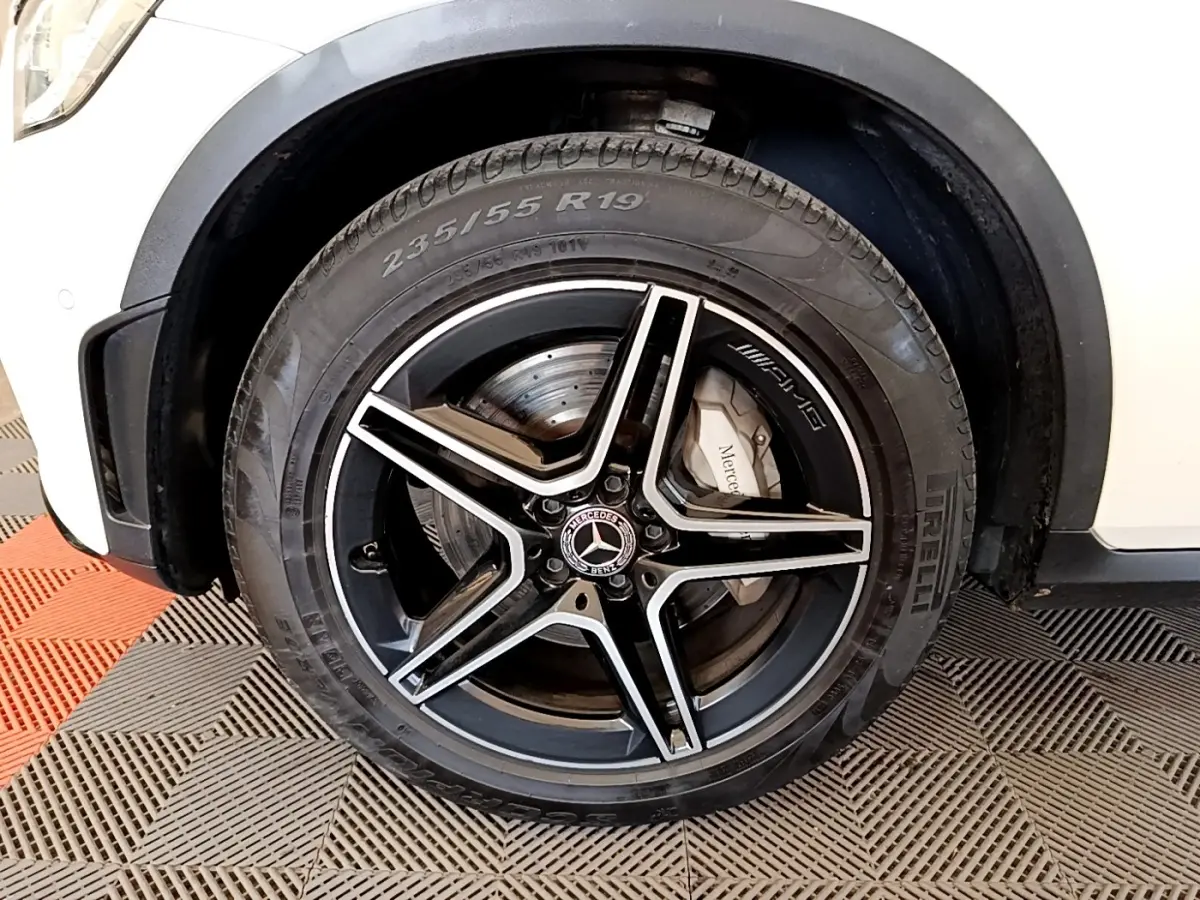 Gros plan sur la roue avant gauche noire et argentée d’un Mercedes GLC 300 e AMG Line blanc, avec logo AMG visible.