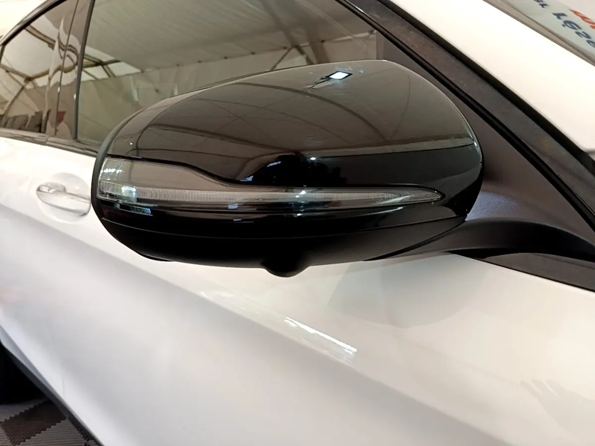 Gros plan sur le rétroviseur noir côté gauche d’un Mercedes GLC Coupé blanc, avec clignotant intégré.