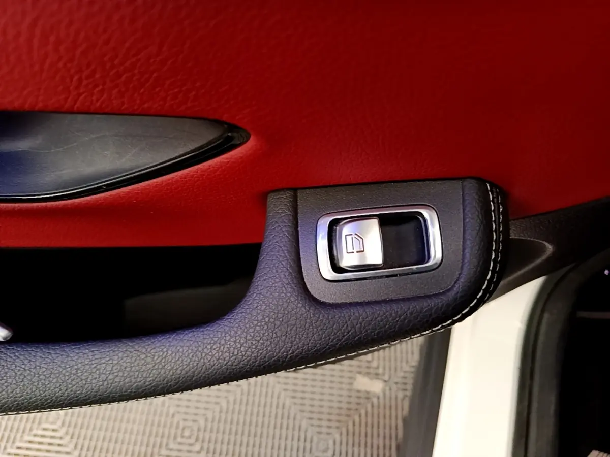 Gros plan sur la poignée intérieure noire avec bouton de vitre, contreporte rouge du Mercedes GLC Coupé blanc 2020.