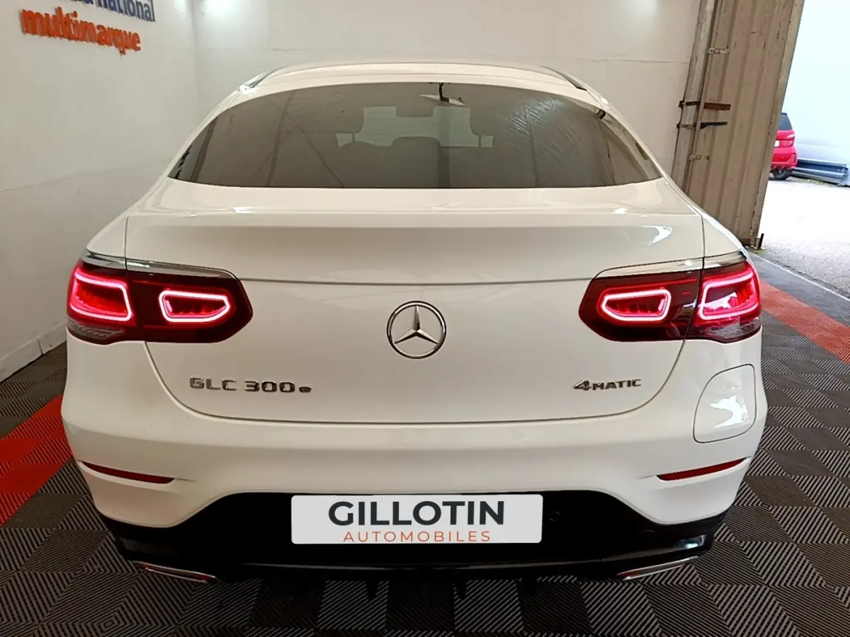 Vue arrière d'un Mercedes GLC 300 e AMG Line 4Matic blanc avec feux LED allumés en intérieur showroom.