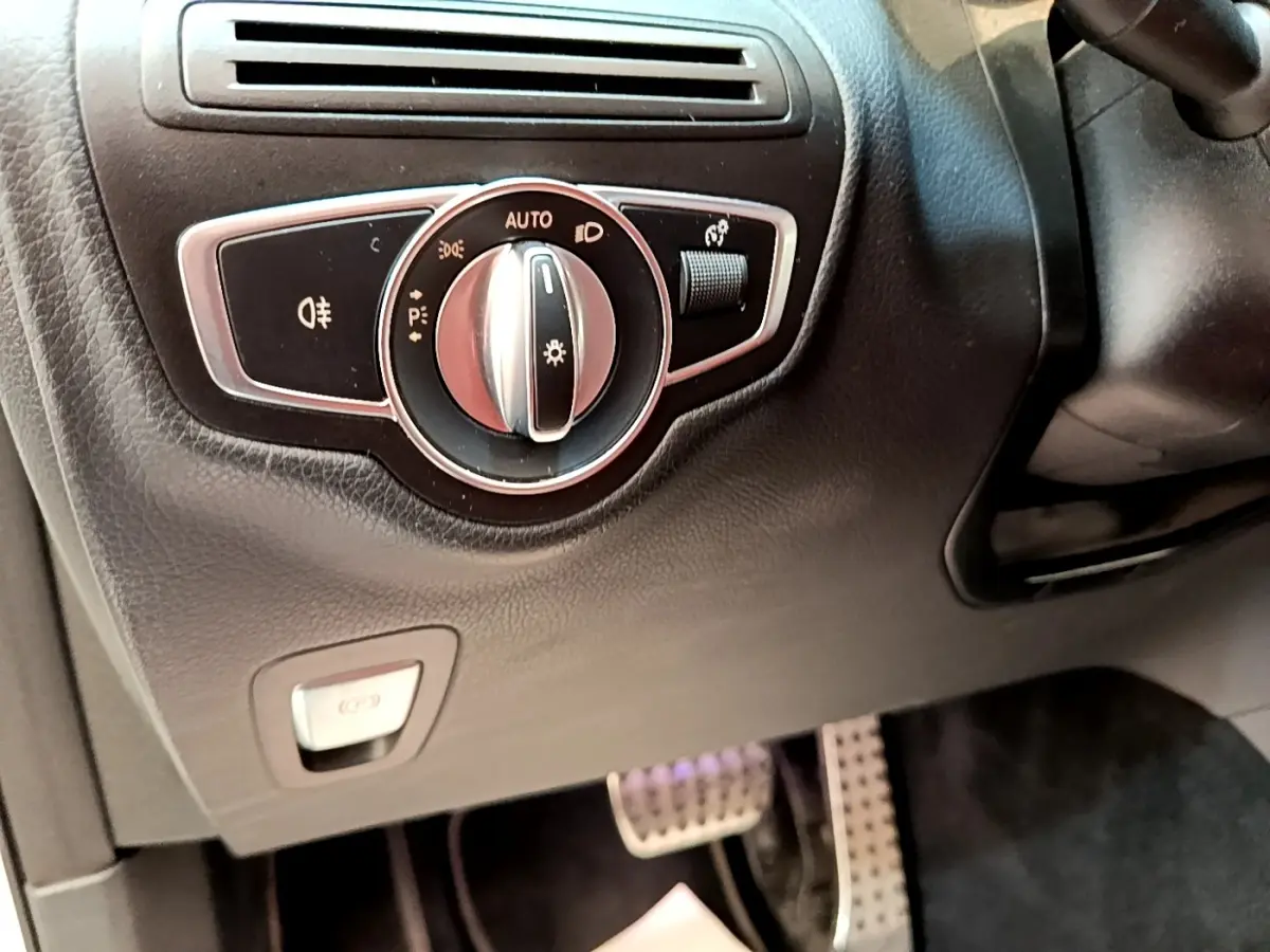 Gros plan sur la commande des phares et frein à main électrique côté gauche du tableau de bord du Mercedes GLC 300 e AMG Line blanc.