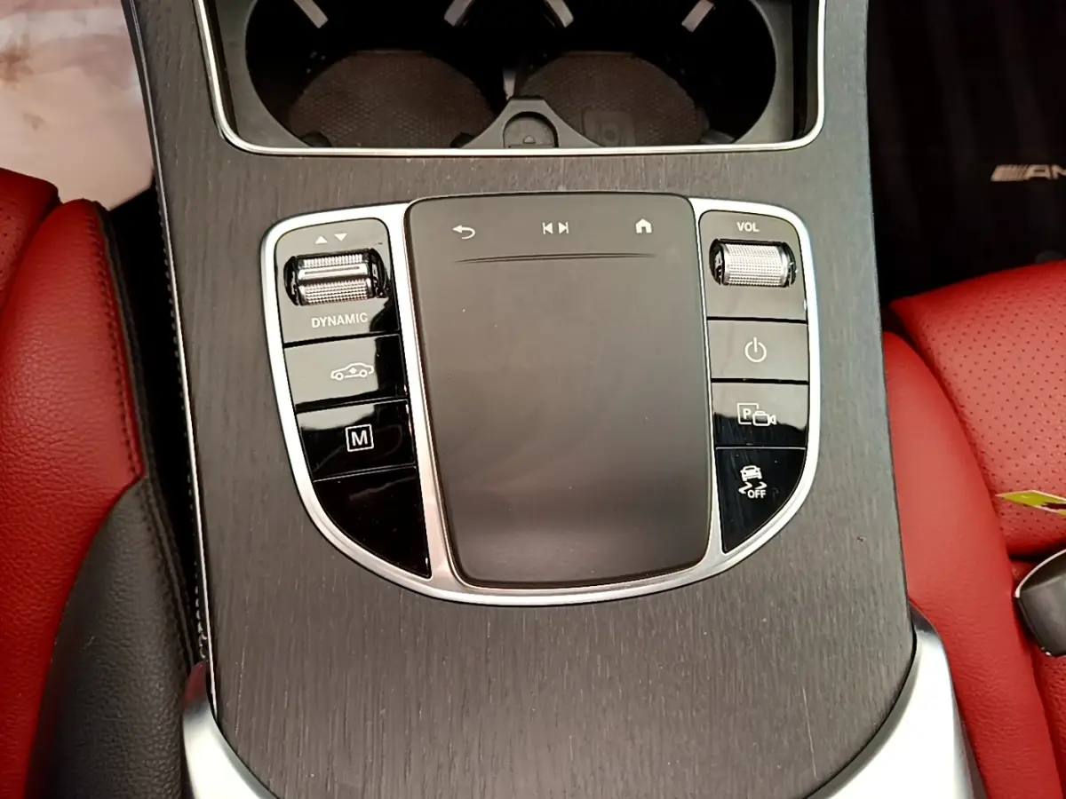 Gros plan sur la console centrale en bois avec commandes tactiles et sièges cuir rouge du Mercedes GLC 300 e AMG Line.