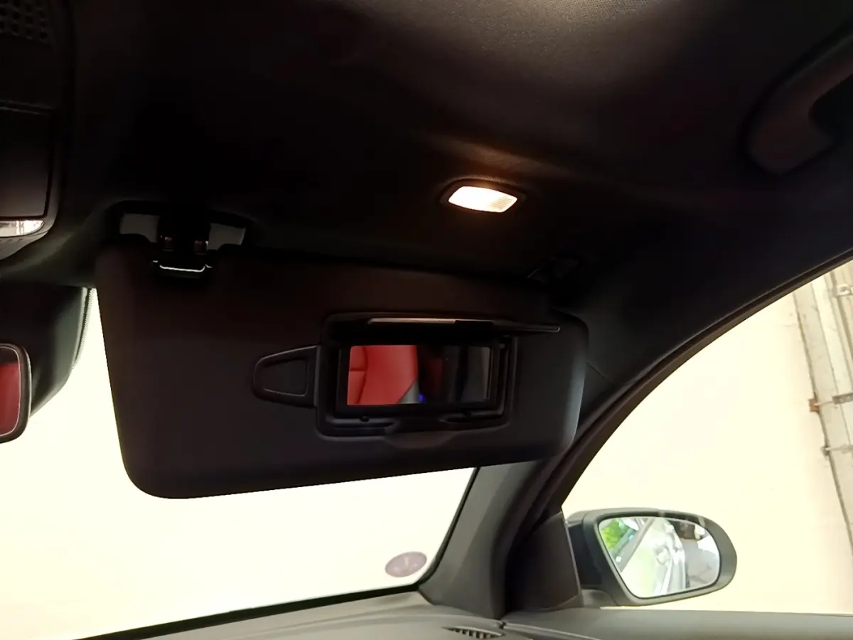 Intérieur du Mercedes GLC Coupé 300 e AMG Line 2020, vue du pare-soleil côté conducteur avec miroir éclairé et siège rouge en reflet.