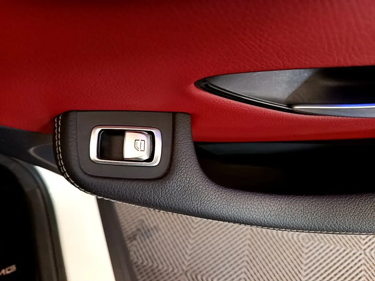 Gros plan sur la poignée intérieure noire et bouton de lève-vitre, avec garniture rouge du panneau de porte du Mercedes GLC Coupé blanc.