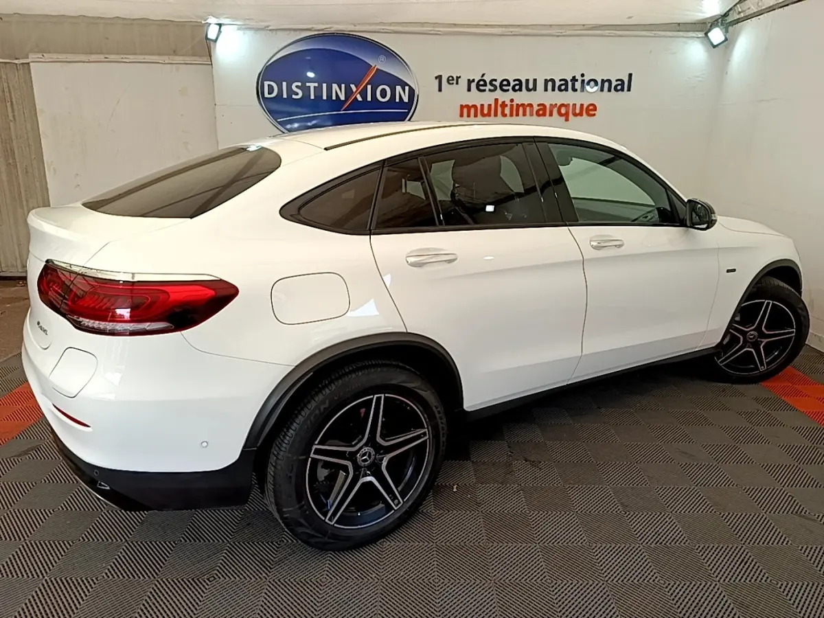 Vue 3/4 arrière droite d'un Mercedes GLC Coupé blanc avec jantes AMG noires et vitres teintées en intérieur showroom.