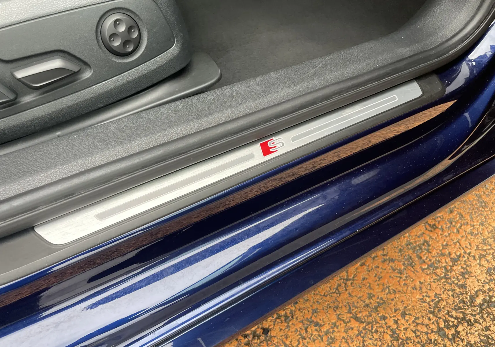Gros plan sur le seuil de porte côté conducteur d'une Audi S4 bleu Navarre avec logo S rouge visible.