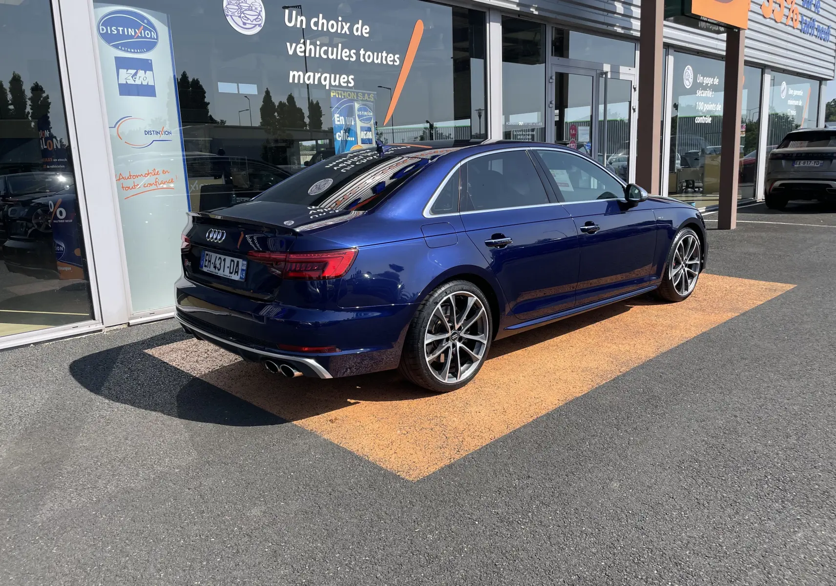 Audi S4 bleu Navarre vue 3/4 arrière droit, avec jantes alliage et double sortie d'échappement chromée, stationnée devant un showroom.
