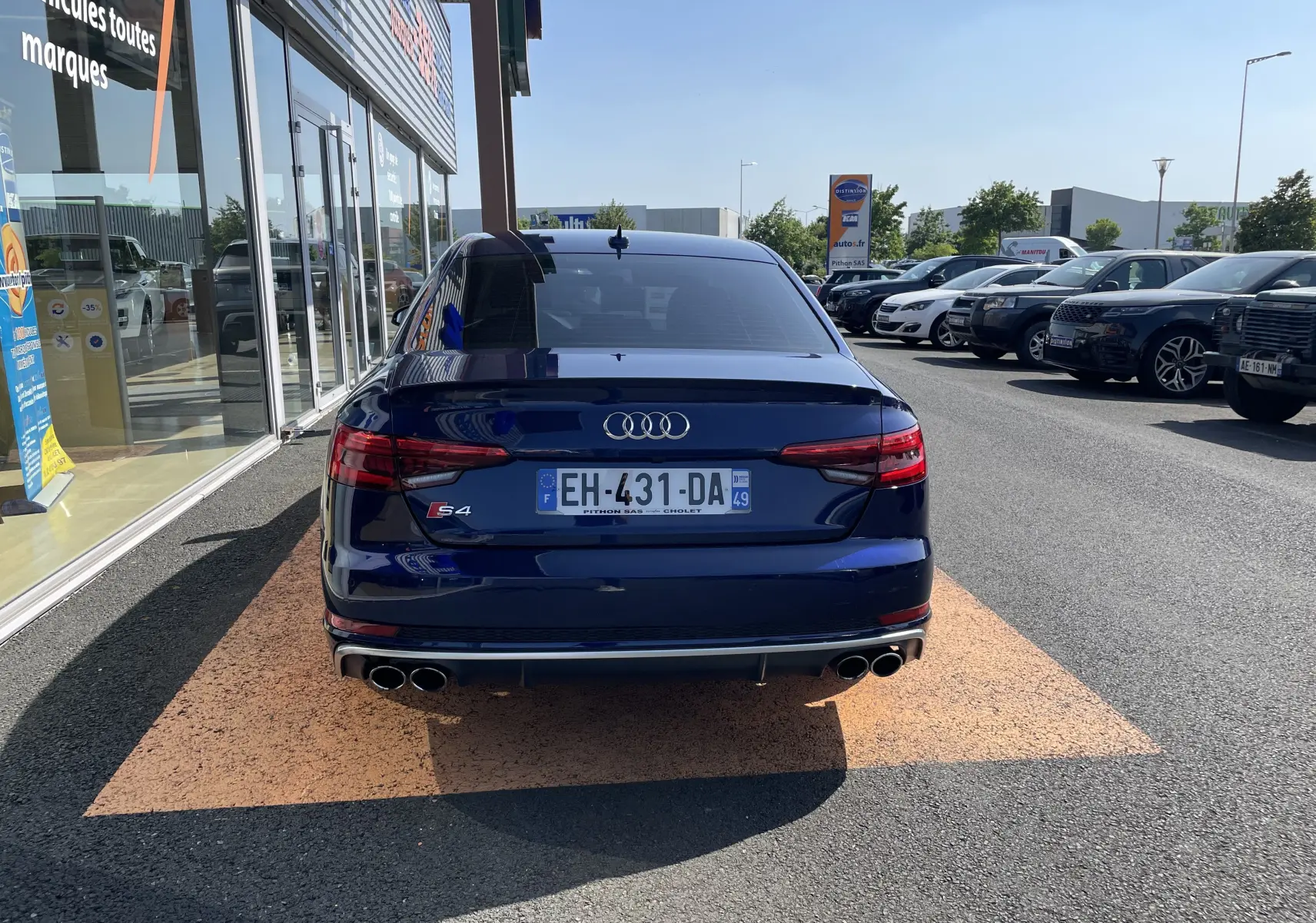 Vue arrière d'une Audi S4 bleu Navarre garée devant un showroom, avec ses quatre sorties d'échappement visibles.