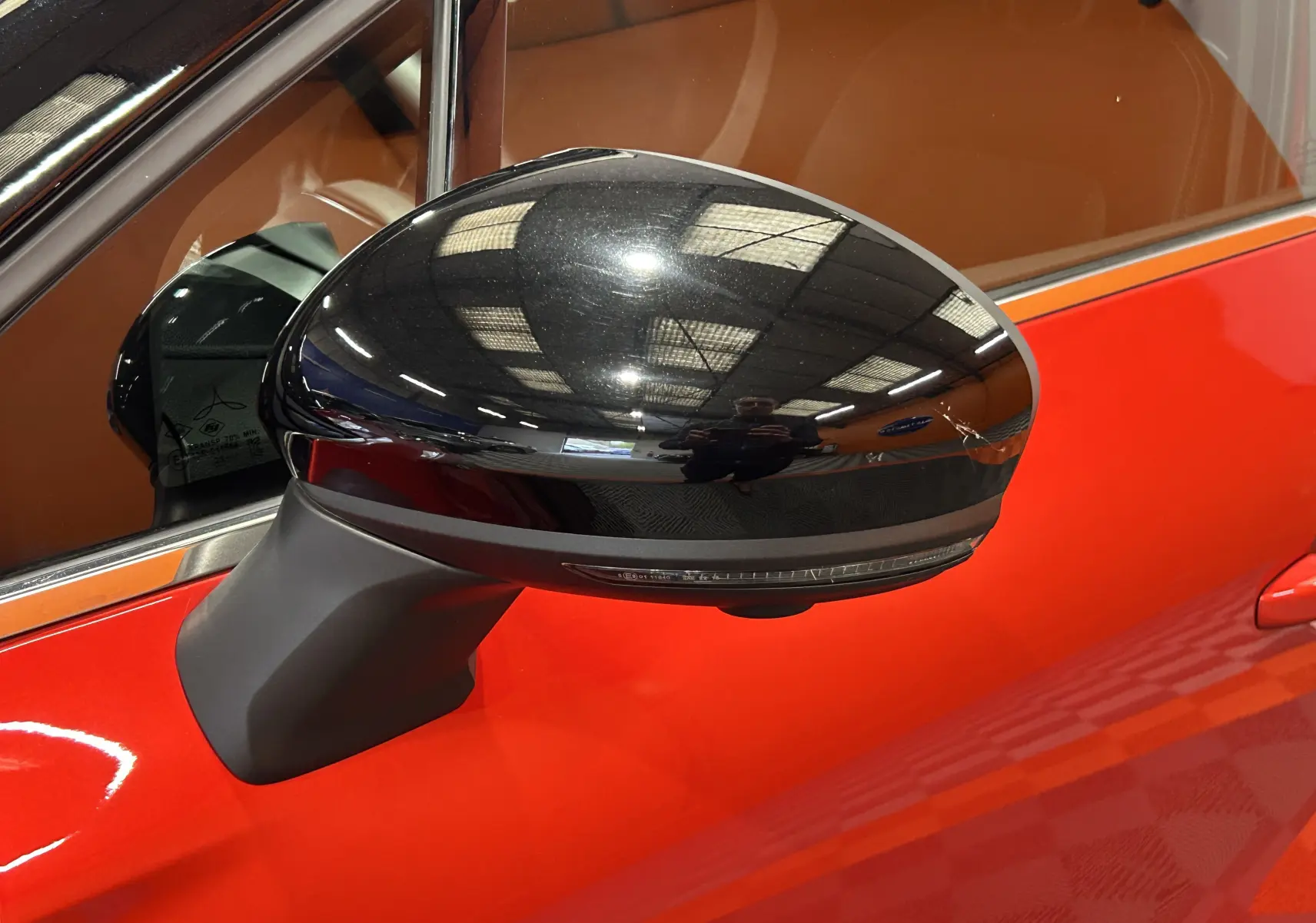 Rétroviseur noir brillant côté gauche du Renault Captur rouge flamme métal 2024 avec intérieur marron visible.