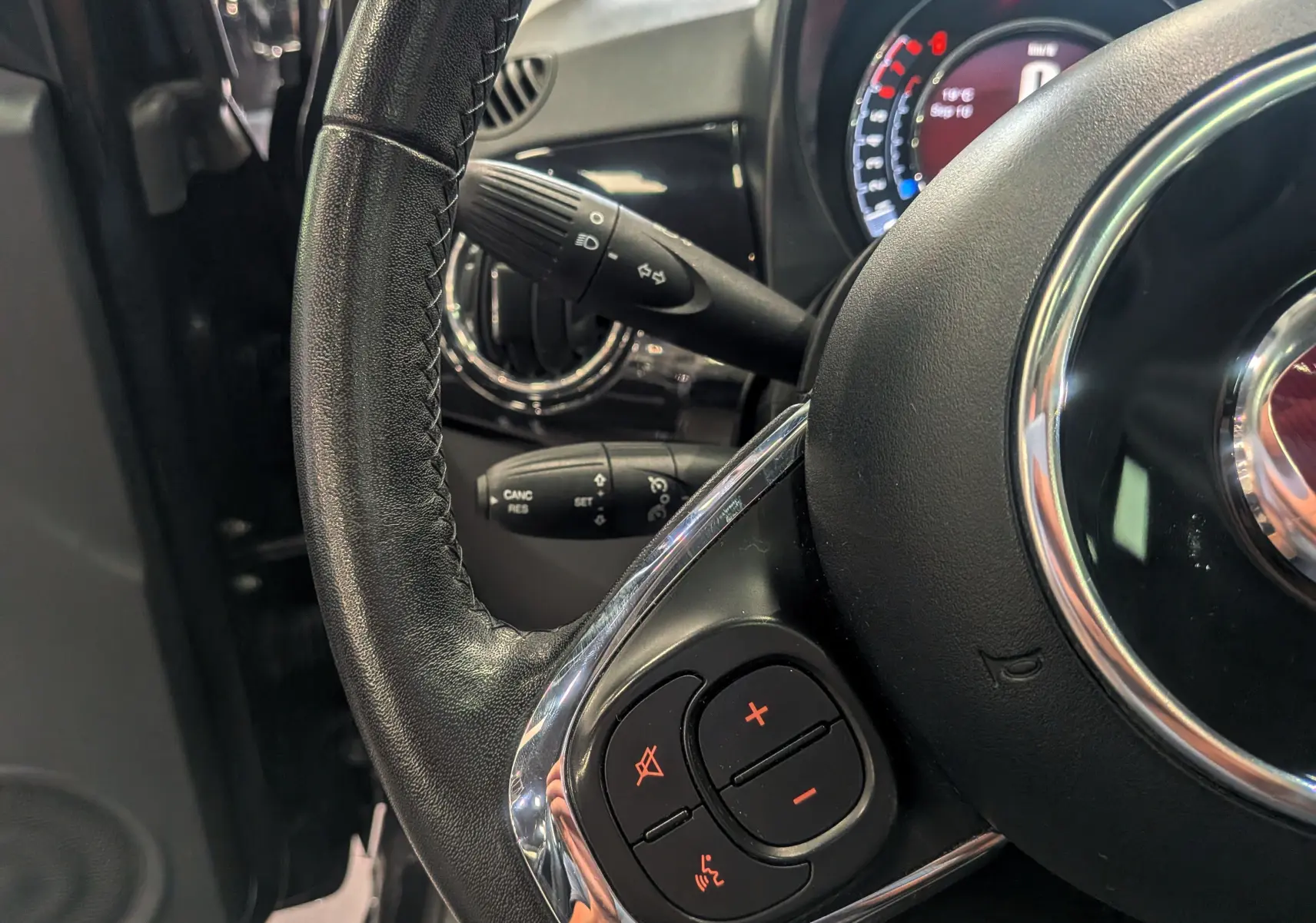 Gros plan sur le volant en cuir noir de la Fiat 500 1.2 69 CH Lounge, avec commandes audio intégrées et tableau de bord en arrière-plan.