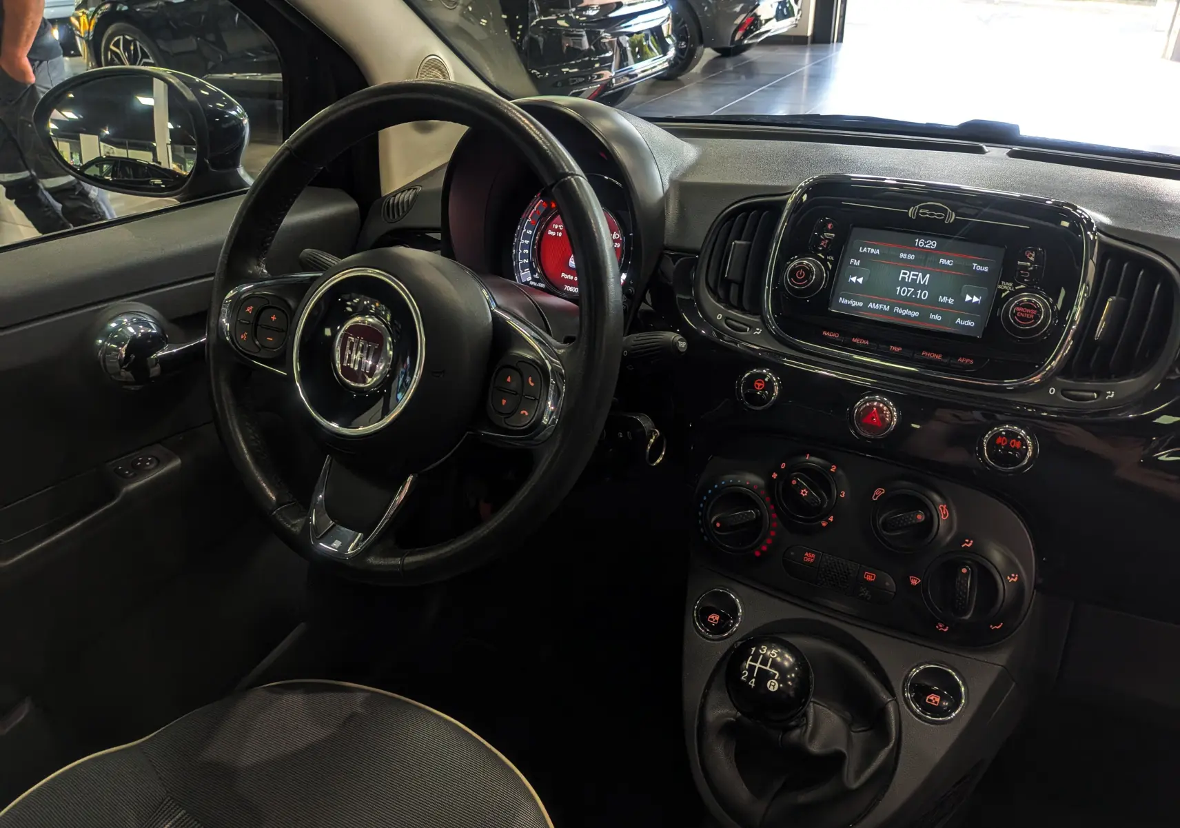 Vue intérieure côté conducteur de la Fiat 500 1.2 69 CH Lounge noire, avec volant multifonction et tableau de bord lumineux.